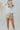 Frontal view of the Going For Gold Mini Skirt that features a gold metallic coloring, a thick waist band with adjustable ties, a tiered design, and a shorts lining.