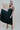 Frontal view of the Stealing Hearts Midi Dress that features a black colored silk material, a surplice neckline, a sleeveless design with thin adjustable straps, a pleated skirt, an open back with crossover straps and adjustable ties, and a midi length