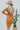 Back view of model wearing the Slipped Away Mini Dress in Camel, that has a camel colored knit material, a surplice neckline, long sleeves, ruched side detailing with adjustable strings, a side slit, a midi length, and a tight fit