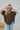 Frontal view of the Bare It All Top that features a brown chiffon material, a multi-colored floral print, a collar neck, a hidden button-up front, a short sleeve, a curved bottom hem side slits, and a high-low design.