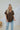 Frontal view of the Bare It All Top that features a brown chiffon material, a multi-colored floral print, a collar neck, a hidden button-up front, a short sleeve, a curved bottom hem side slits, and a high-low design.