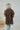 Back view of the Bare It All Top that features a brown chiffon material, a multi-colored floral print, a collar neck, a hidden button-up front, a short sleeve, a curved bottom hem side slits, and a high-low design.
