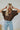 Frontal view of the Bare It All Top that features a brown chiffon material, a multi-colored floral print, a collar neck, a hidden button-up front, a short sleeve, a curved bottom hem side slits, and a high-low design.