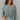 Frontal view of the Easy Breezy Top that features a green colored knit material, an open knit design, a V neckline, a long cuffed sleeve, side slits, and a high-low design.
