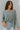 Frontal view of the Easy Breezy Top that features a green colored knit material, an open knit design, a V neckline, a long cuffed sleeve, side slits, and a high-low design.
