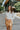 Frontal view of the Serenity Sweater that features a cream colored knit material, a high neckline, long cuffed sleeves, a surplice front with a tie closure, a side chest cut-out, and a thick bottom hem.