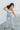 Back view of the Signature 8: Crossed Paths Jeans that features a medium wash denim, a front button and zipper closure, crossover waist line, two front pockets, distressing through out, a raw bottom hem, two back pockets, and a wide leg fit.