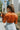 Back view of the Falling For You Top that features a rust colored silk material, a collar neck, a surplice front with a wrap tie closure, and long sleeves with feather detail at the hem.