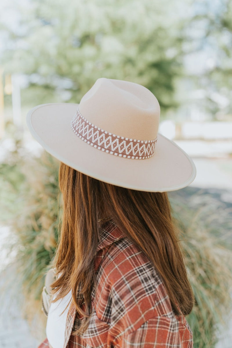 The Heading South Hat is a wide brim hat featuring a khaki fabric, a brown and white aztec pattern belt, and adjustable ties within for different fits.