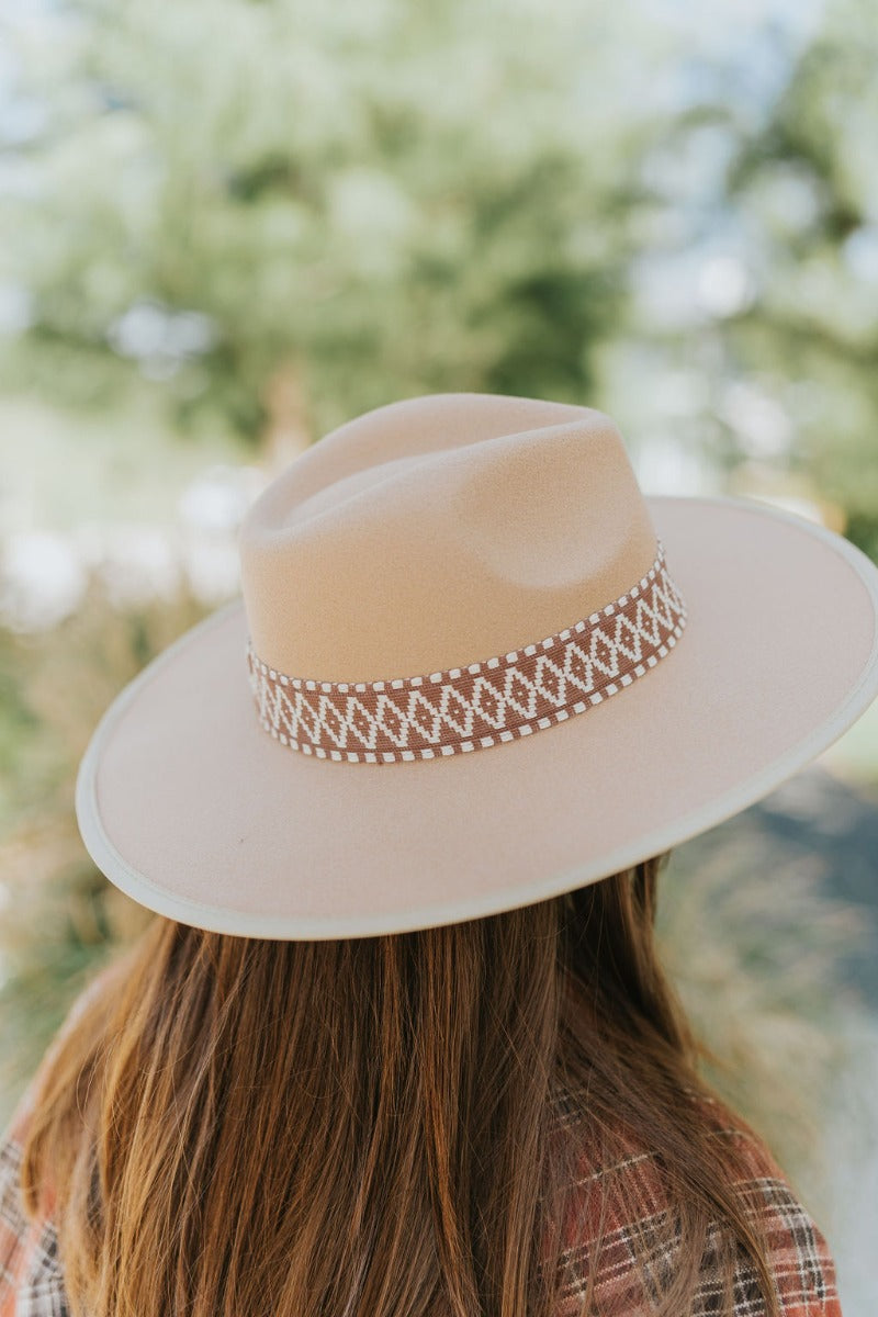 The Heading South Hat is a wide brim hat featuring a khaki fabric, a brown and white aztec pattern belt, and adjustable ties within for different fits.