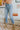 Front view of model wearing the Ceros: Fast Forward Jeans, that have medium wash denim, a front button and zipper closure, two front pockets, a distressed bottom hem, two back pockets, and a straight leg fit.