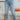 Front view of model wearing the Ceros: Fast Forward Jeans, that have medium wash denim, a front button and zipper closure, two front pockets, a distressed bottom hem, two back pockets, and a straight leg fit.