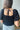 Close up/back view of model wearing the Stand Alone Top which features a black material, a scoop neckline with a ruffle hem, a short puffy sleeve, a smocked front, a flowy bottom he, a cropped fit, a smocked back, and a tie back.