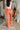 Back view of model wearing the Weekend Lover Pants which features orange satin fabric, two front pockets, a front zipper with hook closure, and flared legs.