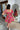 Back view of model wearing the Best Memory Floral Dress which features hot pink, light pink, orange, yellow green and white fabric with a floral and gingham pattern, ruffle trim, a mini length hem, pink lining, a sweetheart neckline, a smocked back, and s