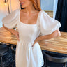 Close up view of model wearing the In This Moment Dress which features white fabric with a white lining, short puff sleeves with elastic trim, a back tie, and a side zipper closure.
