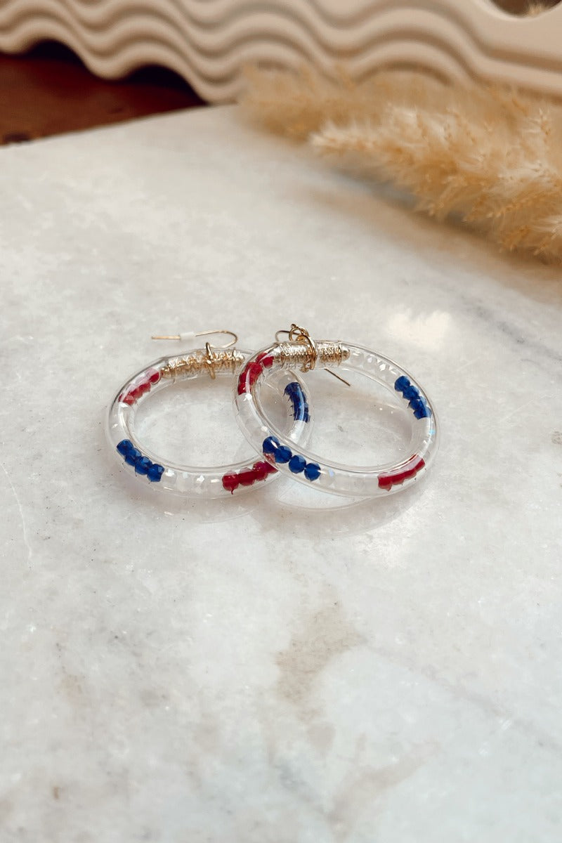 The American Honey Hoop Earring features blue, red and white beads in a clear circle tube and gold hardware.