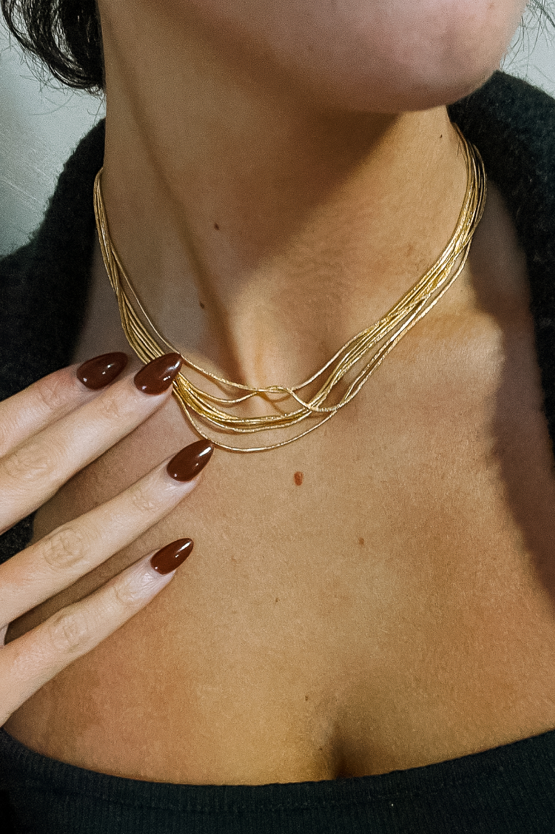 Close up view of model wearing the Nora Gold Layered Necklace which features seven, gold, skinny, slinky, layers with adjustable clasp closure.
