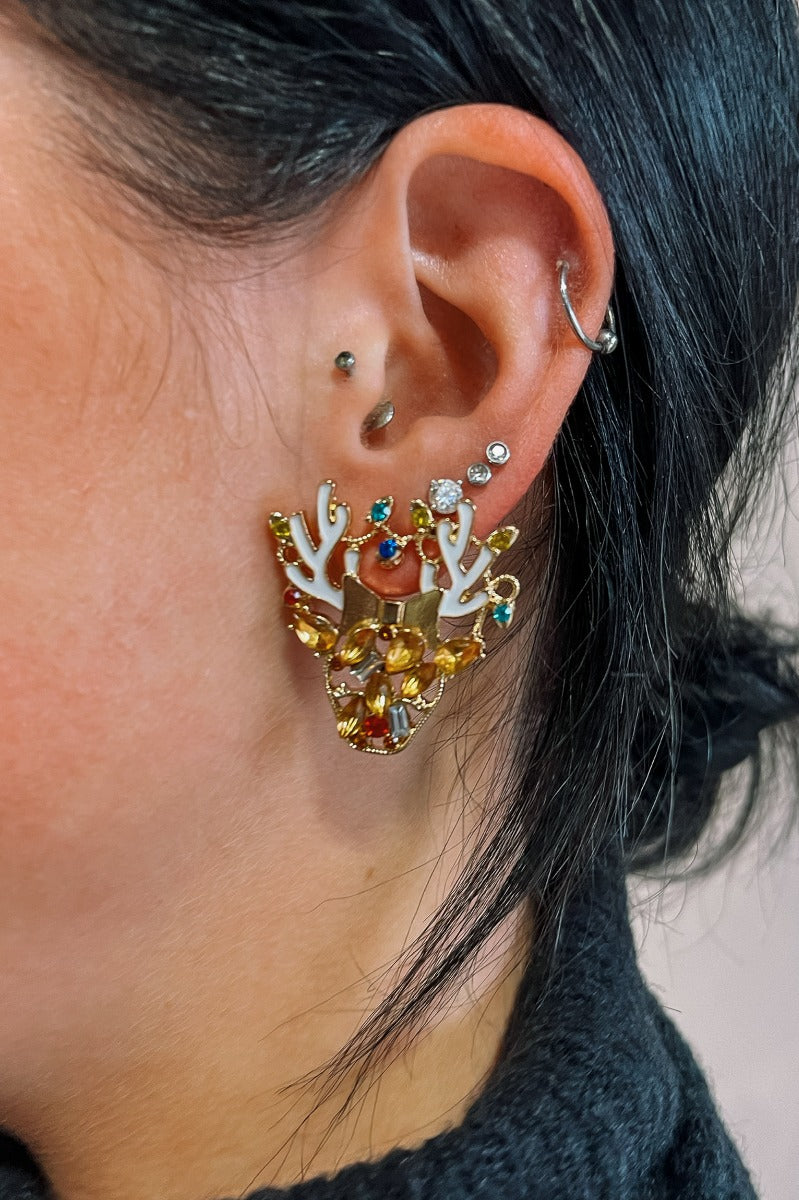 Close up of model wearing the Reindeer Gold Multi Stone Earrings that feature gold reindeer shaped studs with white antlers and multi color stones.