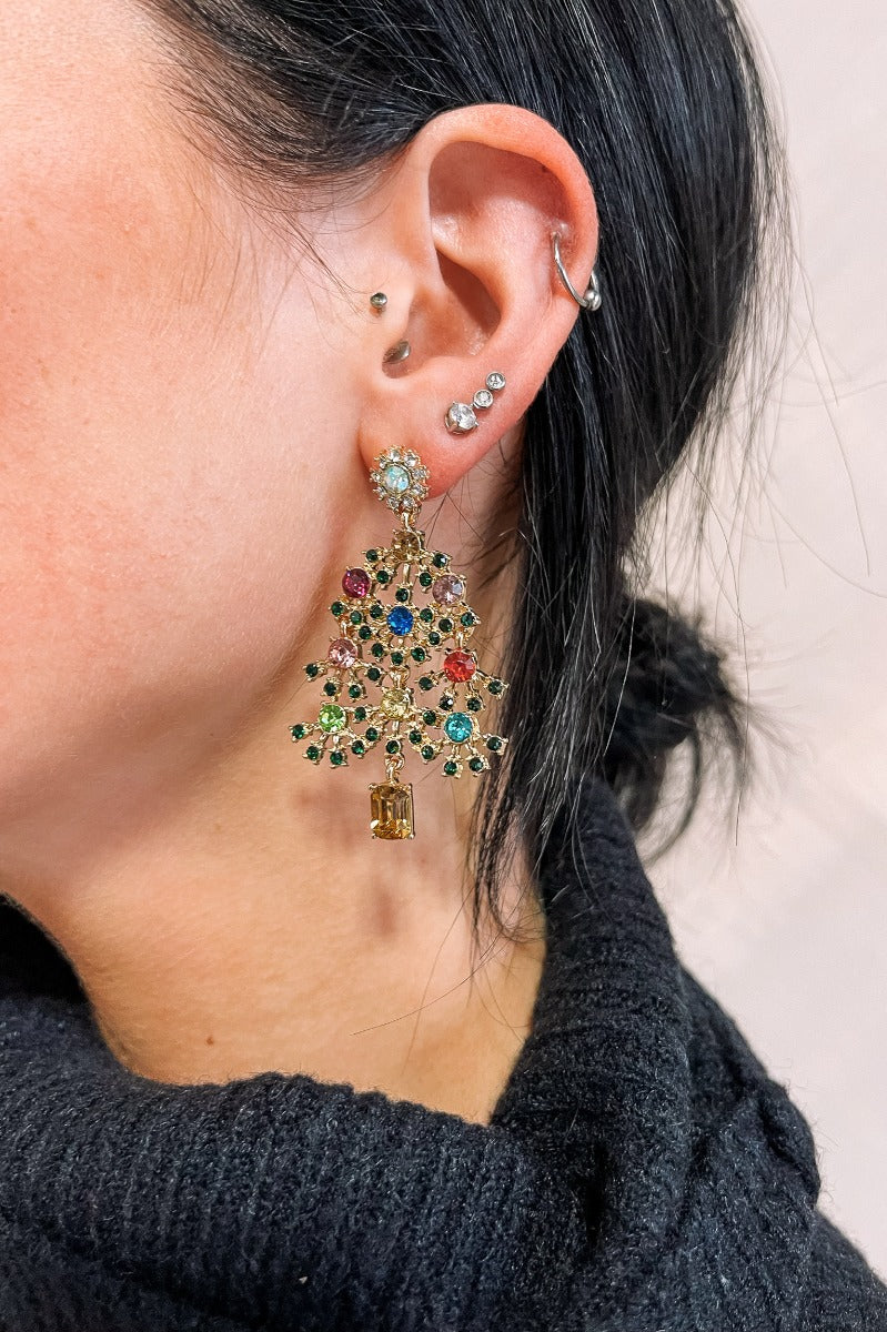 Side view of model wearing the Anastasia Christmas Tree Earrings that feature dangle christmas trees set in gold with multi color stones.