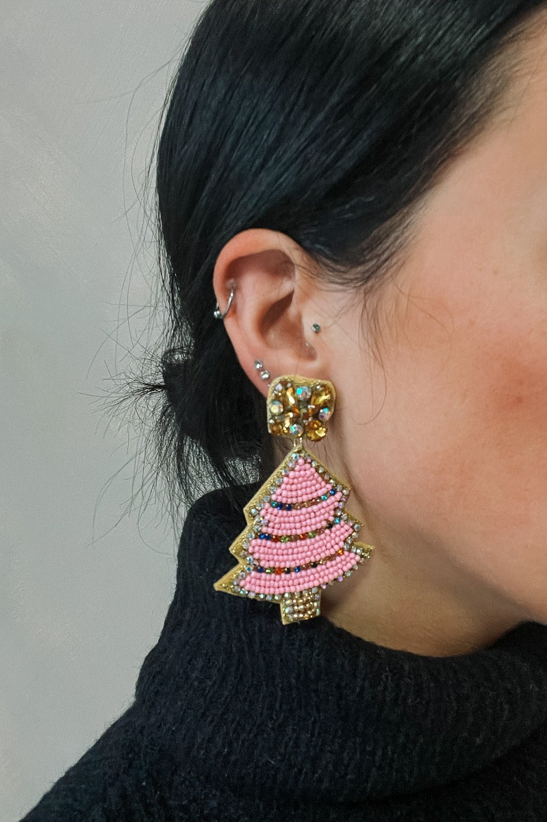 Side view of model wearing the Sara Pink Beaded Christmas Tree Earrings that have christmas tree shaped dangle earrings with pink, amber and irredescent stones with gold trim details.