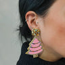Side view of model wearing the Sara Pink Beaded Christmas Tree Earrings that have christmas tree shaped dangle earrings with pink, amber and irredescent stones with gold trim details.