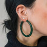 Close side view of model wearing the Carmen Emerald Stone Hoop Earrings that feature large closed hoops with emerald green stones.
