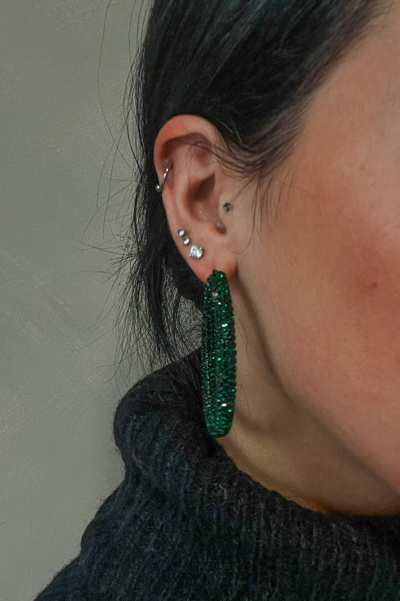 Close view of model wearing the Carmen Emerald Stone Hoop Earrings that feature large closed hoops with emerald green stones.