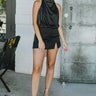 Front view of model wearing the Call Me Later Satin Skort that has black satin fabric, a small front slit, black shorts lining, and a monochromatic back zipper with a hook closure.
