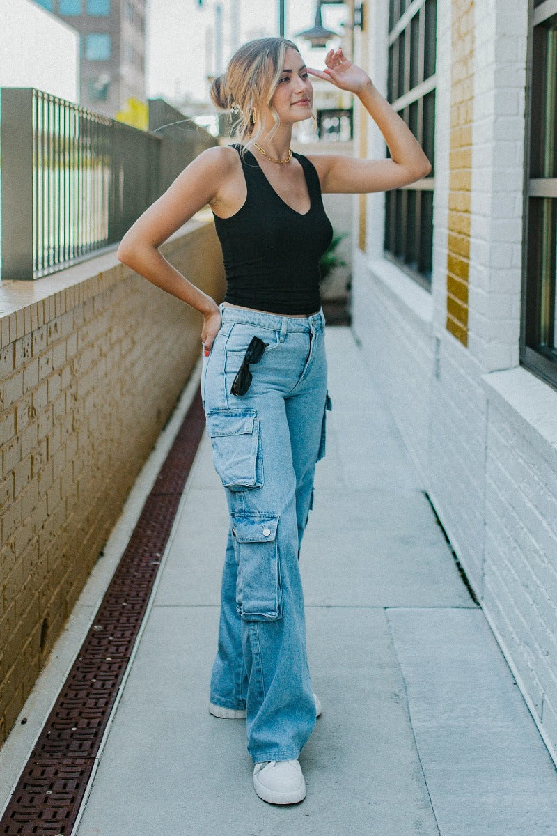 Side view of model wearing the Dakota Cargo Jeans that have blue denim fabric, pockets, a front zipper with a button closure, belt loops and wide legs