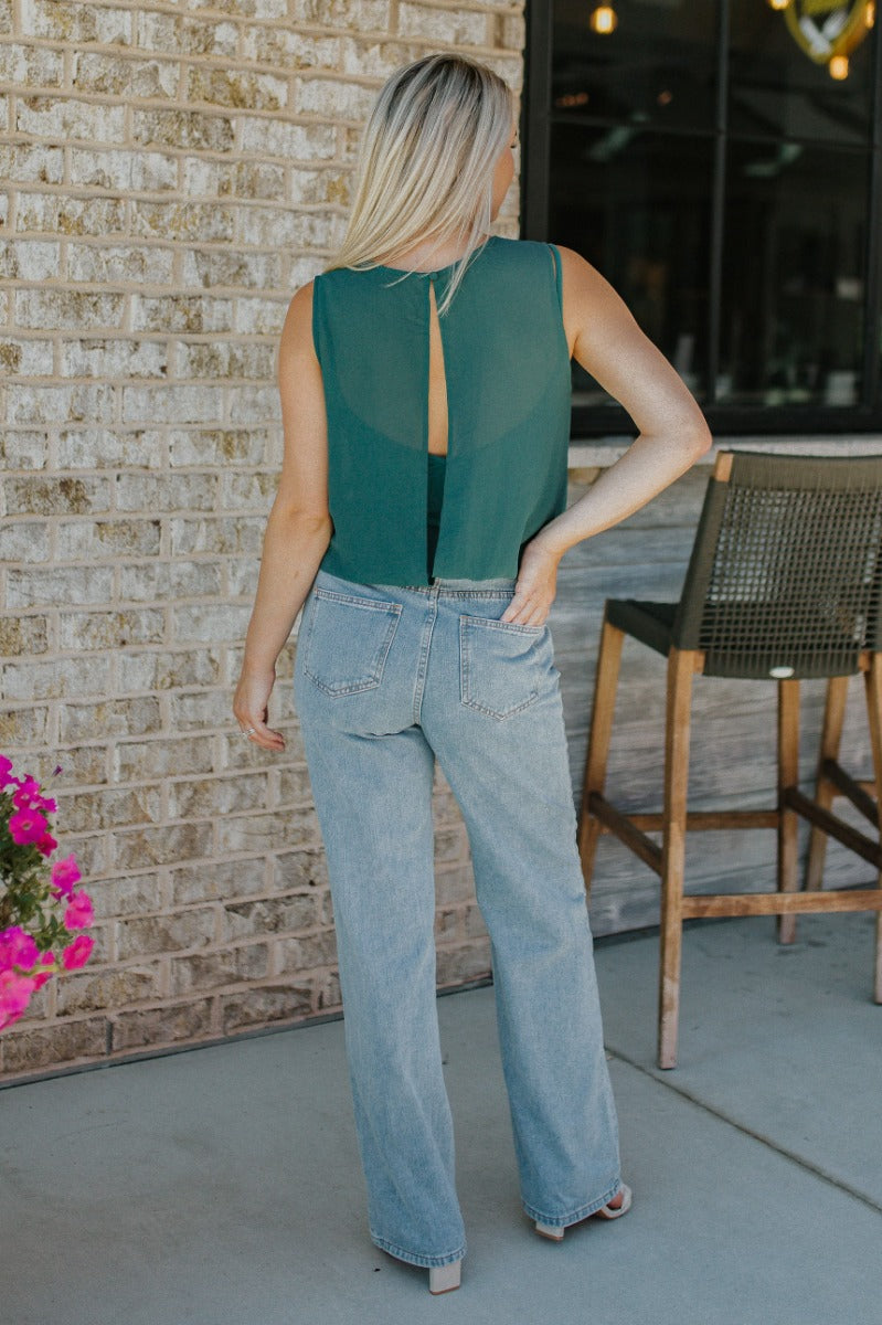 Back view of model wearing the Brentwood Wide Leg Jeans that have medium wash denim fabric, brown stitching, a front zipper with a button closure, two front pockets, two back pockets, belt loops and wide legs.