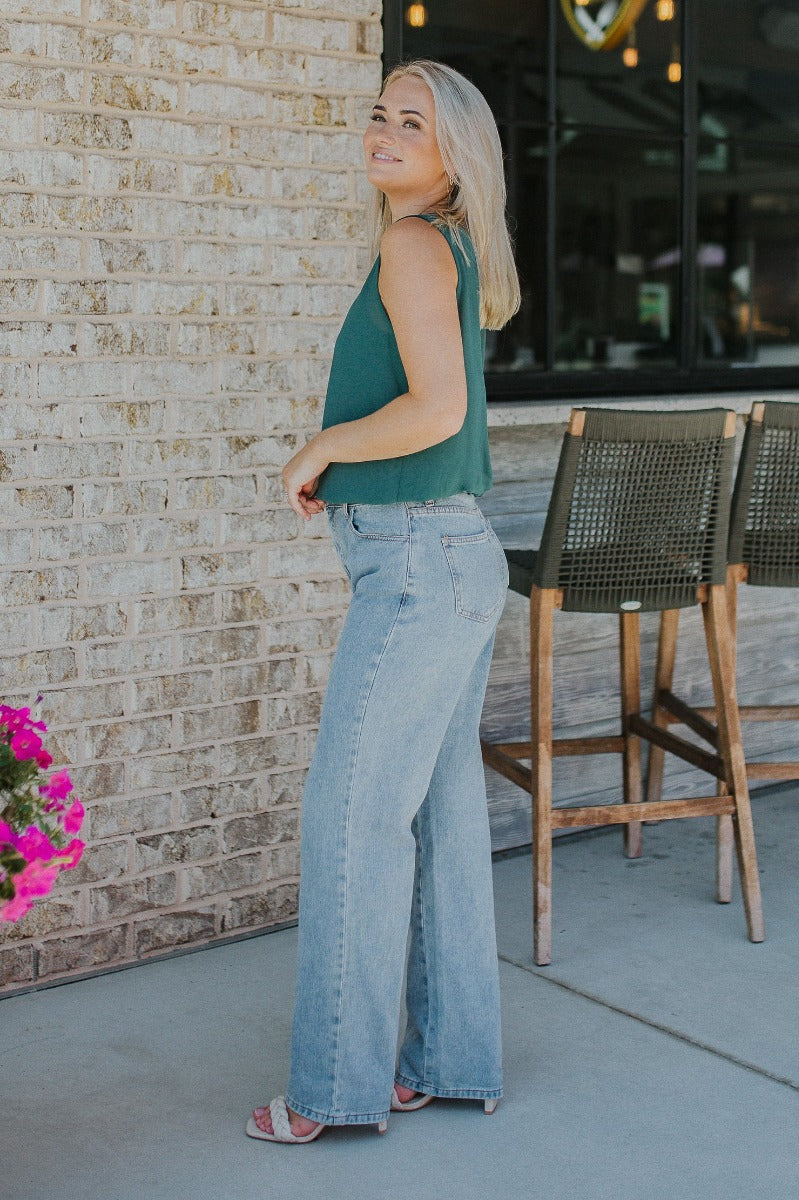 Side view of model wearing the Brentwood Wide Leg Jeans that have medium wash denim fabric, brown stitching, a front zipper with a button closure, two front pockets, two back pockets, belt loops and wide legs.