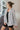 Front view of model wearing the Hayden Plaid Top that has cream fabric with a dark grey stripe plaid, white tortoise buttons, a collared neck, front chest pocket, dropped shoulders and long sleeves.