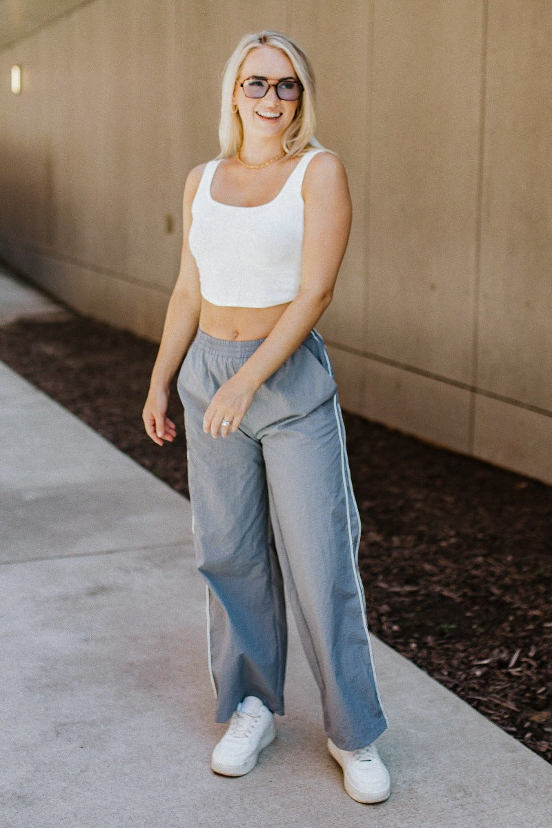 Full body front view of model wearing the Ready To Go Pants that have grey lightweight fabric, white stripe side details, an elastic waistband, two front pockets and straight leg pants