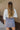 Back view of model wearing the Bring It On Skirt that has grey lightweight fabric, two front pockets with drawstring ties, mini length and an elastic waistband with drawstring ties