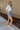 Full body side view of model wearing the Bring It On Skirt that has grey lightweight fabric, two front pockets with drawstring ties, mini length and an elastic waistband with drawstring ties