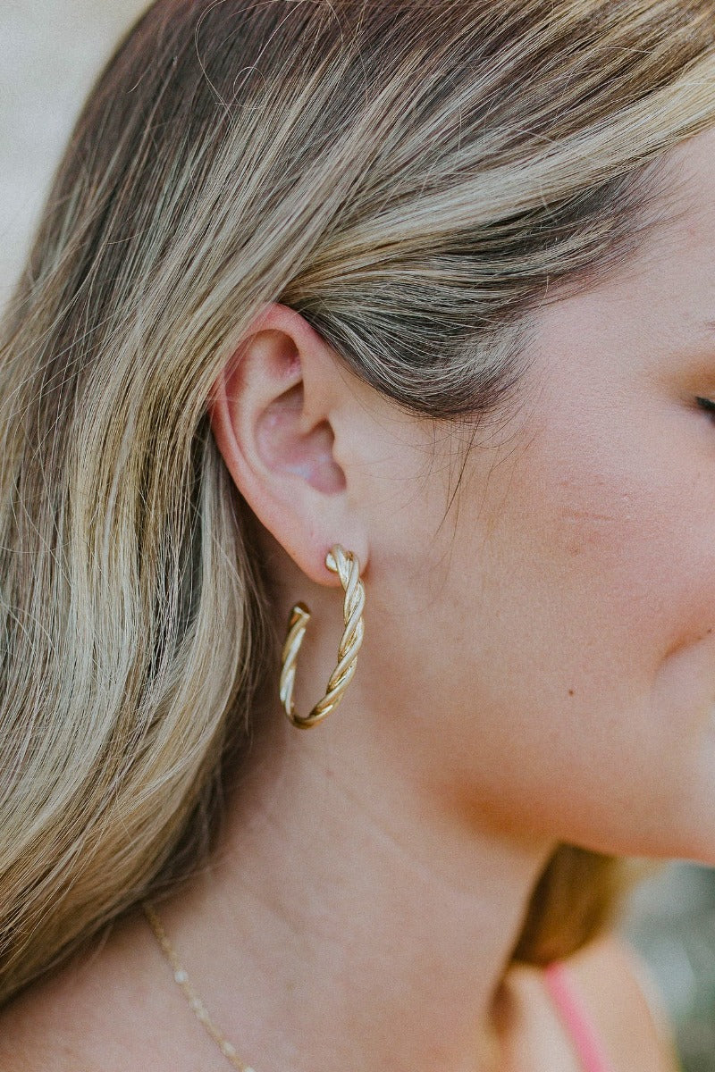 Side view of model wearing the Full of Spirit Hoops which features medium, open hoops with gold rope design.