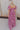 Full body back view of model wearing the Falling For You Floral Dress which features berry pink, purple, green and white sheer fabric, floral print, berry pink lining, front slit, ruffle layered hem, sweetheart neckline, short puff sleeve with ruffle hem 
