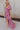 Full body side view of model wearing the Falling For You Floral Dress which features berry pink, purple, green and white sheer fabric, floral print, berry pink lining, front slit, ruffle layered hem, sweetheart neckline, short puff sleeve with ruffle hem 
