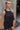 Frontal side view of model wearing the All Over Again Romper which features black lightweight fabric, shorts lining, tiered ruffle design, round neckline, sleeveless and monochromatic back zipper with hook closure.