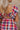 Close up back view of model wearing the Ever So Sweet Dress which features orange, pink, navy blue, purple, white and brown knit fabric, plaid pattern, white lining, mini length, pockets on each side, plunge neckline, ruffle elastic straps and open back w