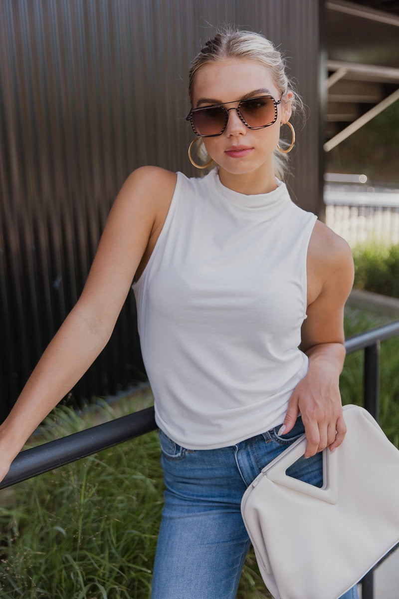 front view of model wearing the True Story Mock Neck Tank in White that has white knit fabric, a high neckline, and a sleeveless design.