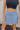 Front view of model wearing the Step It Up Skort in Denim which features dusty blue fabric, shorts lining, a v overlap waistline, slits on each side, and a mini-length hem.