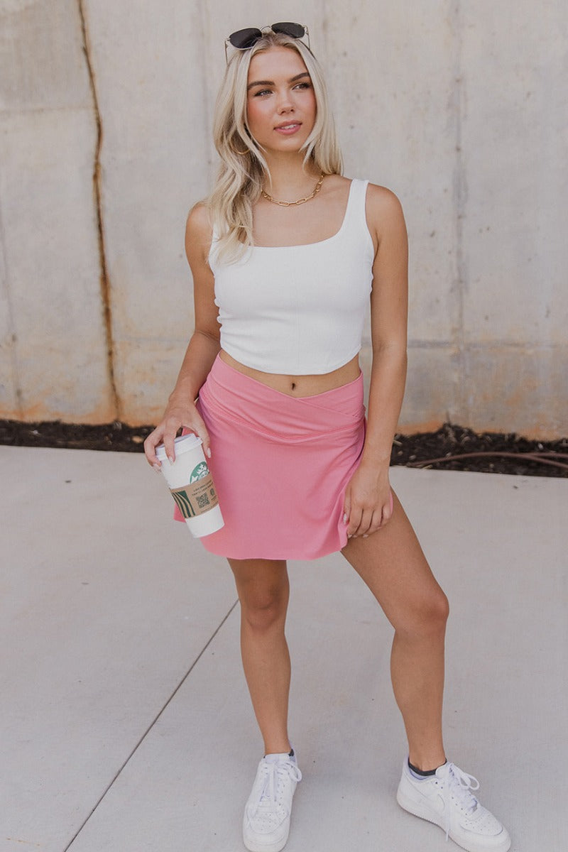 Full body view of model wearing the Step It Up Skort in Rose which features rose pink fabric, shorts lining, a v overlap waistline, slits on each side, and a mini-length hem.