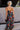 Full body back view of model wearing the Beautiful Mess Floral Dress which features black, orange, fuchsia, teal, aqua, green and white fabric, floral print, midi dress, two-tiered body, square neckline, adjustable straps and monochromatic back zipper wit