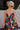 Front view of model wearing the Beautiful Mess Floral Dress which features black, orange, fuchsia, teal, aqua, green and white fabric, floral print, midi dress, two-tiered body, square neckline, adjustable straps and monochromatic back zipper with hook cl