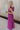 Full body back side view of model wearing the Moment in Time Jumpsuit which features plum lightweight fabric, plum lining, wide leg pants, criss cross detail at waist, plunge neckline, ruffle straps, corset ties in the back, open back and monochromatic ba