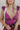 Close up view of model wearing the Moment in Time Jumpsuit which features plum lightweight fabric, plum lining, wide leg pants, criss cross detail at waist, plunge neckline, ruffle straps, corset ties in the back, open back and monochromatic back zipper w