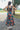 Back view of model wearing the Daydreamer Midi Dress in Hunter Green that has hunter green fabric with peach, light pink, purple, blue and olive geometric pattern, midi, smocked upper, square neck, and elastic straps.