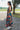 Side view of model wearing the Daydreamer Midi Dress in Hunter Green that has hunter green fabric with peach, light pink, purple, blue and olive geometric pattern, midi, smocked upper, square neck, and elastic straps.